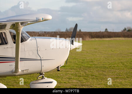 Close up vue détaillée de l'avant d'un avion léger à hélice en stationnement sur le bord d'un pays de l'herbe l'aérodrome de côté. Banque D'Images