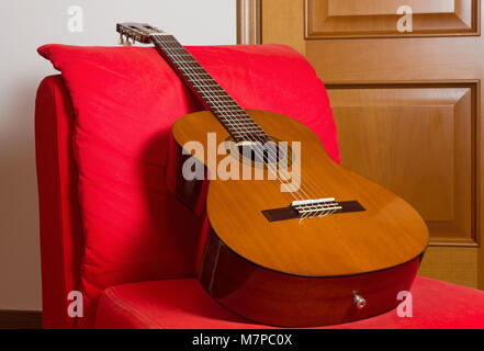 Guitare classique sur un fauteuil rouge avec une porte en bois à l'arrière-plan Banque D'Images