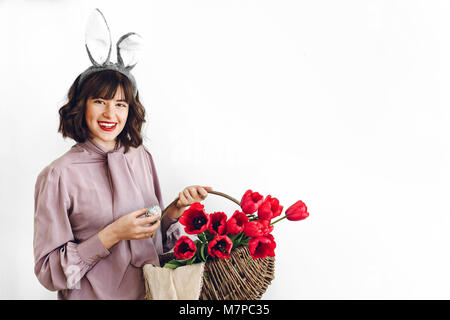 Concept de recherche de pâques. belle fille élégante en oreilles de lapin holding basket avec des tulipes roses et les oeufs de pâques sur fond blanc isolated.happy woman hol Banque D'Images