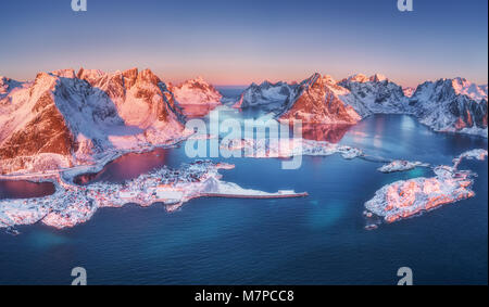 Vue aérienne de Reine et Hamnoy au lever du soleil en hiver. Les îles Lofoten, Norvège. Paysage panoramique avec bleu de la mer, montagnes enneigées, de hautes roches, village Banque D'Images
