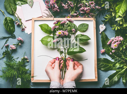 Female florist mains attachés avec des fleurs bouquet de corde avec des feuilles vertes sur l'espace de travail avec le bac blanc et le papier blanc, carte Vue de dessus Banque D'Images