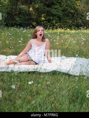 Une jeune femme le bâillement dans un champ de fleurs. Banque D'Images