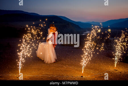 Mariage romantique tourné du baiser de jeunes mariés. Le marié est levée la mariée sur les montagnes décorées avec des brûlures d'artifice. Banque D'Images