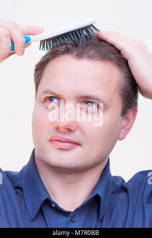Portrait of young Caucasian man with blue shirt ethnie peigner les cheveux de brossage avec brosse sur fond blanc Banque D'Images