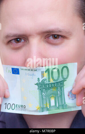 Close-up portrait of young Caucasian man ethnicité couvrant la bouche avec de l'argent d'un billet de cent euros Banque D'Images