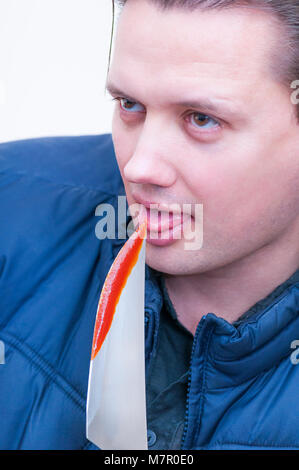 Close-up portrait of young Caucasian man ethnicité léchant le sang de dégustation à partir de la pointe d'un couteau sur fond blanc Banque D'Images