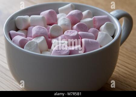 Tasse blanche contenant des guimauves miniatures rose et blanc sur la surface de chêne Banque D'Images