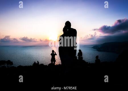 Les gens qui suivent le coucher du soleil sur la plage. Vue arrière d'un couple regardant silhouette soleil au coucher du soleil sur la plage avec un éclairage chaleureux. Banque D'Images
