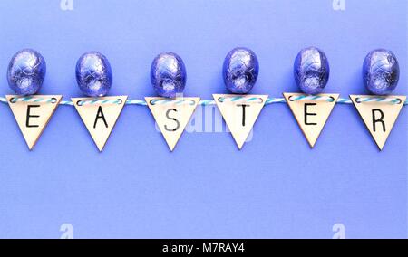 Creative concept Pâques avec des oeufs en chocolat violet enveloppé. avec le mot Easter, fabriqué à partir de triangles en bois de couleur violet. backgroun Banque D'Images