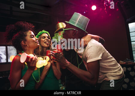 Group of cheerful friends having fun at bar. Les hommes multi-ethnique et les femmes à faire la fête et danser au night club. La célébration de la Saint-Patrick. Banque D'Images