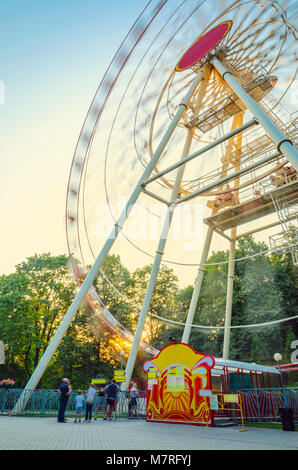 Silhouettes floues en mouvement de personnes se tenant dans la ligne de la Grande Roue dans le parc d'amusement au coucher du soleil. Une longue exposition Paysage dans l'amusemen Banque D'Images