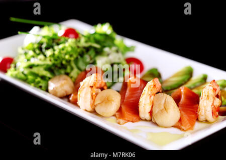 Sur une plaque blanche un mélange de salade avec des tranches de saumon crevettes et seaux de mer. Décoration avec de l'avocat avec la sauce soja et de cerise Banque D'Images