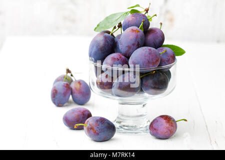 Les prunes mûres fraîches dans un bol en verre sur fond blanc Banque D'Images