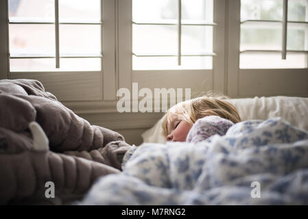 Petit enfant endormi dans un lit confortable avec fenêtre douce lumière pendant la journée Banque D'Images