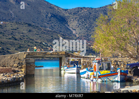 Le célèbre canal d'Elounda avec les ruines de l'ancien pont, bateaux de pêche et un groupe de jeunes nageurs d'hiver, Crète, Grèce Banque D'Images