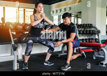 Young Asian woman doing fitness squat l'exercice dans la salle de sport avec un entraîneur personnel. Banque D'Images
