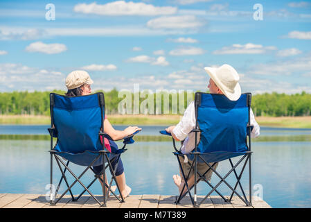 Vue depuis l'arrière d'un couple sur des chaises relaxe près d'un lac sur une jetée en bois Banque D'Images