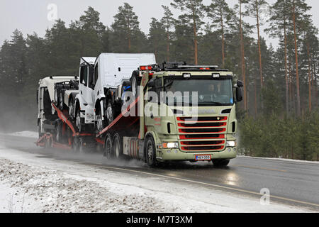 SALO, FINLANDE - le 9 mars 2018 : Véhicule Scania camion transporteur de MotorTrans transporte trois nouveaux camions lourds sur route mouillée dans la neige dans le sud de la Finlande. Banque D'Images