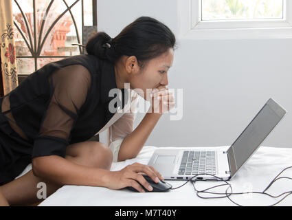 Une jeune femme travaillant sur son ordinateur portable sur le lit. Une jeune fille écrit sur l'ordinateur dans la chambre. Banque D'Images