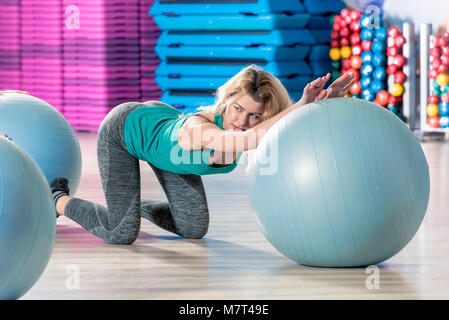 Fille, c'est engagé sur un ballon de gymnastique, s'intéresse à l'entraîneur, tire dans la salle de sport Banque D'Images