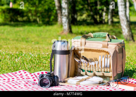 Une bouteille thermos avec des ustensiles, un thermos avec du thé et un appareil photo sur une nappe dans le parc Banque D'Images