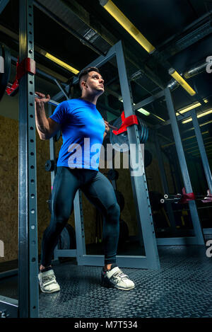 Beau male bodybuilder avec un lourd barbell posant dans la salle de sport Banque D'Images