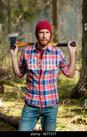 Forester barbu sévère avec une hache dans la forêt portrait vertical Banque D'Images