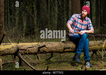 Portrait d'un forestier dans une chemise à carreaux avec une hache assis sur un journal Banque D'Images Portrait d'un forestier dans une chemise à carreaux avec une hache assis sur un journal Banque D'Images
