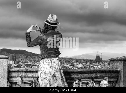 Soirée parfaite avec vue magnifique. Vus de derrière, voyageur élégant femme en robe et chapeau de paille à Barcelone, Espagne montrant la main en forme de coeur Banque D'Images