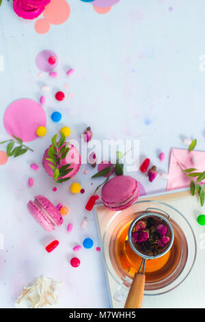 Glas verre gros plan sur un fond en bois clair avec Macaron Pistache rose cookies, feuilles, des bonbons durs, des bonbons et de copier l'espace. Banque D'Images