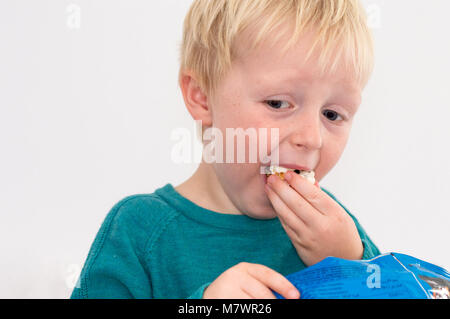 Didim, Turquie - 01 octobre 2017 : Sweet garçon blond aux yeux bleus de manger un sac de popcorn devant un fond blanc. Banque D'Images