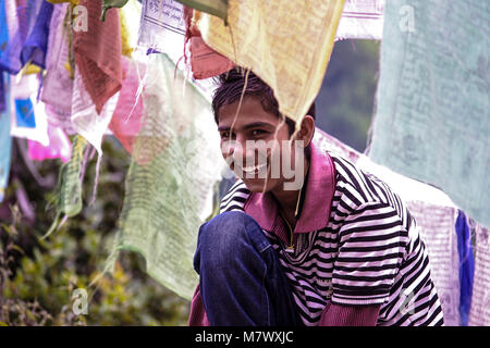 Jeune homme assis sous les drapeaux de prières colouful sur un sentier de randonnée au Tiger's Nest monastère, Paro, Bhoutan. Les drapeaux de prières sont communs dans l'himalaya Banque D'Images