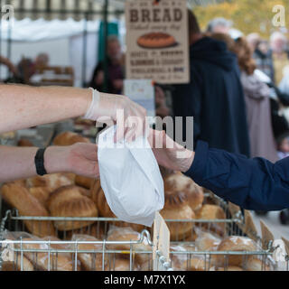 L'homme vend du pain pour femme en sac de papier à partir de la boulangerie échoppe de marché tout en portant des gants de caoutchouc pour maintenir l'hygiène alimentaire Banque D'Images