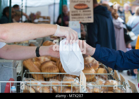 L'homme vend du pain pour femme en sac de papier à partir de la boulangerie échoppe de marché tout en portant des gants de caoutchouc pour maintenir l'hygiène alimentaire Banque D'Images