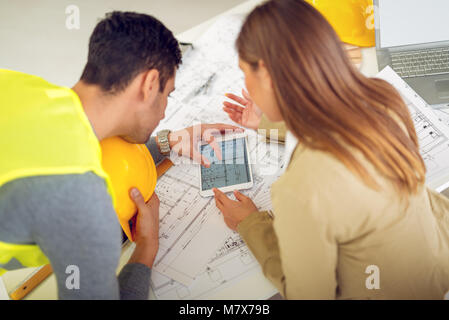 Les jeunes architectes contrôle les plans architecturaux sur tablette dans le bureau, discuter et planifier ce qu'il faut changer pour être mieux. Vue arrière. Banque D'Images