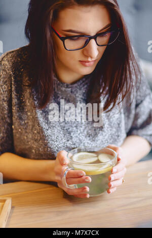 Le thé chaud avec du citron en délicats women's hands au café Banque D'Images