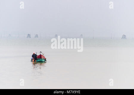 Un pêcheur vietnamien patauge dans les eaux peu profondes pour tirer son bateau de pêche traditionnel de la côte à la ferme ostréicole, Lap un lagon, Vietnam Banque D'Images