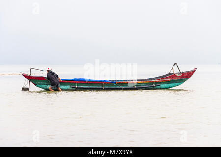 Un pêcheur vietnamien patauge dans les eaux peu profondes pour tirer son bateau de pêche traditionnel de la côte à la ferme ostréicole, Lap un lagon, Vietnam Banque D'Images