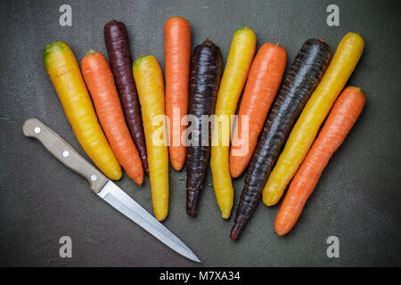 Légumes colorés. Couleur organique jaune, rouge, orange et violet les carottes sur la surface de la pierre sombre. Style rustique Banque D'Images