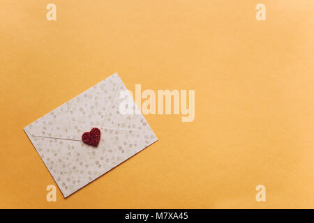 Enveloppe avec un symbole en forme de cœur rouge sur fond jaune. Arrière-plan de célébration. Banque D'Images