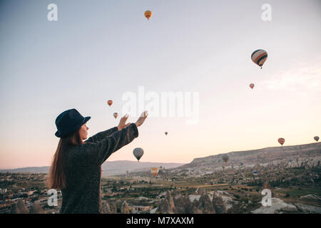 Une fille dans un chapeau admire montgolfières volant dans le ciel au-dessus de la Cappadoce en Turquie. Spectacle impressionnant. Tourisme Banque D'Images