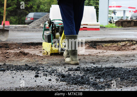 Un travailleur de la construction routière compacte le sol avec un compact vibroplate avant l'asphaltage d'une partie marécageuse problématique de la route. La Russie, l'entrée dans e Banque D'Images