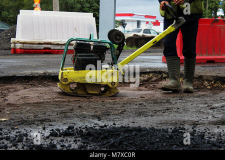 Un travailleur de la construction routière compacte le sol avec un compact vibroplate avant l'asphaltage d'une partie marécageuse problématique de la route. La Russie, l'entrée dans e Banque D'Images