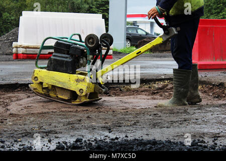 Un travailleur de la construction routière compacte le sol avec un compact vibroplate avant l'asphaltage d'une partie marécageuse problématique de la route. La Russie, l'entrée dans e Banque D'Images