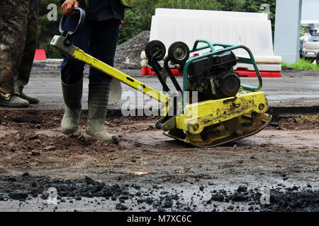 Un travailleur de la construction routière compacte le sol avec un compact vibroplate avant l'asphaltage d'une partie marécageuse problématique de la route. La Russie, l'entrée dans e Banque D'Images