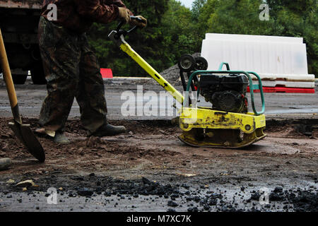 Un travailleur de la construction routière compacte le sol avec un compact vibroplate avant l'asphaltage d'une partie marécageuse problématique de la route. La Russie, l'entrée dans e Banque D'Images