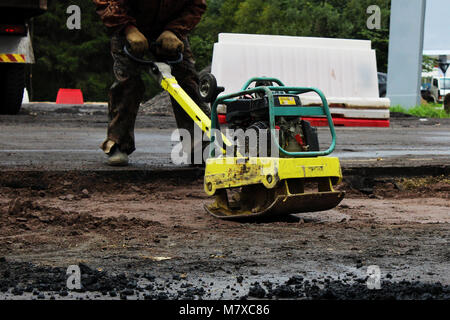 Un travailleur de la construction routière compacte le sol avec un compact vibroplate avant l'asphaltage d'une partie marécageuse problématique de la route. La Russie, l'entrée dans e Banque D'Images