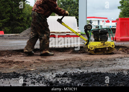 Un travailleur de la construction routière compacte le sol avec un compact vibroplate avant l'asphaltage d'une partie marécageuse problématique de la route. La Russie, l'entrée dans e Banque D'Images