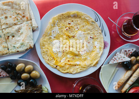 Vue de dessus - omelette, pain, gâteau avec verts, crêpes et assiette de légumes sur la table rouge Banque D'Images