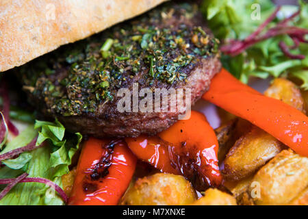 - Burger burger chic sur pain ciabatta avec les quartiers de pommes de terre, poivrons rôtis et salade. Banque D'Images